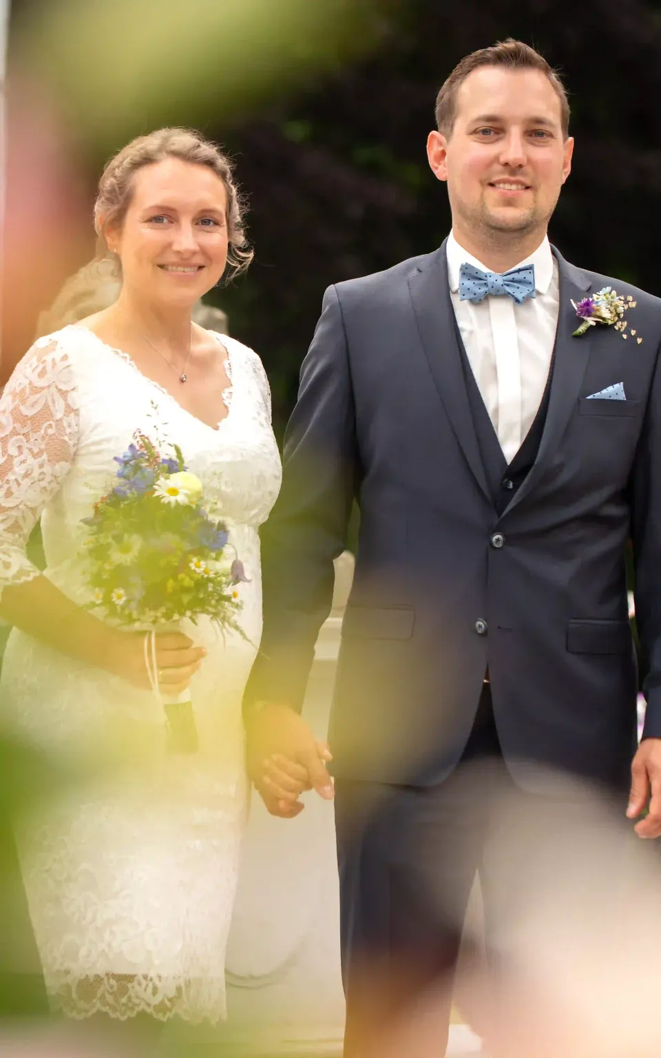 Brautpaar im Freien, fotografiert durch unscharfe Blüten